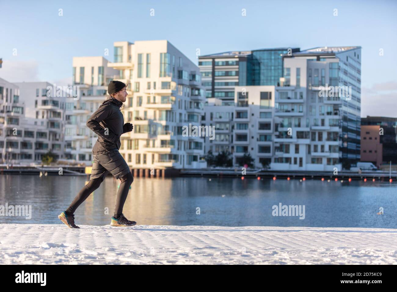 L'atleta di runner della città che corre in inverno fa jogging all'esterno sulla moderna via del porto urbano sul lungomare. Gestione di persone sane e vive attive Foto Stock