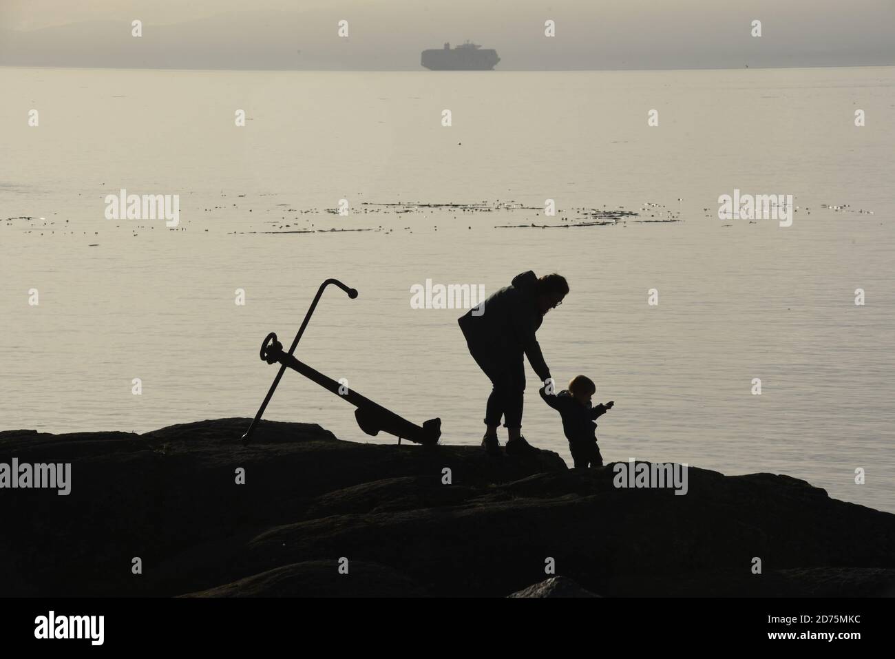 Una donna e un bambino sono silhouette come lei aiuta il ragazzo, discende una roccia in un parco vicino Victoria su Vancouver Island, British Columbia, Canada. Un vecchio s Foto Stock