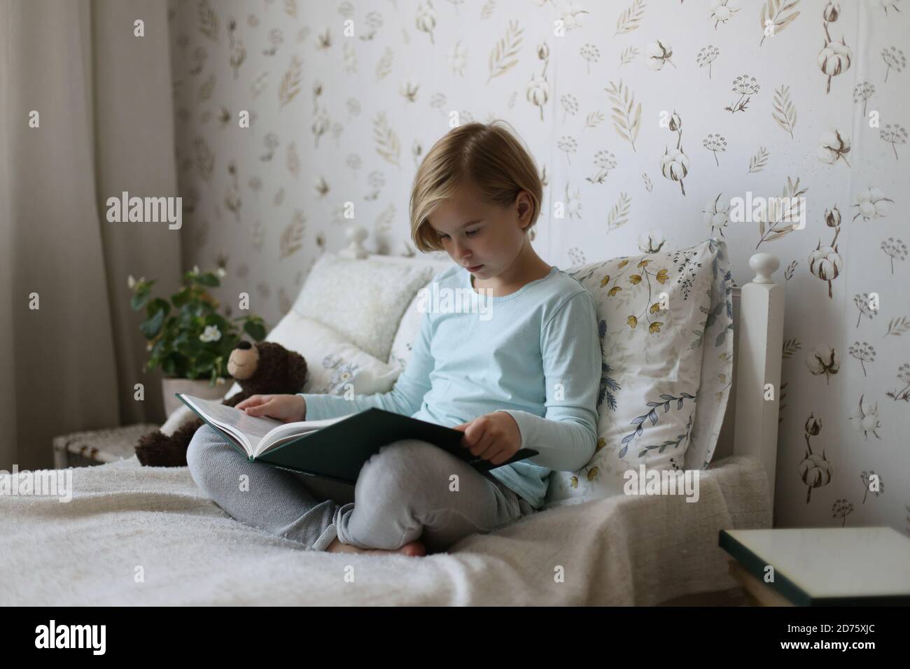 Una ragazza russa sta leggendo un libro sul suo letto in una stanza luminosa. Foto Stock