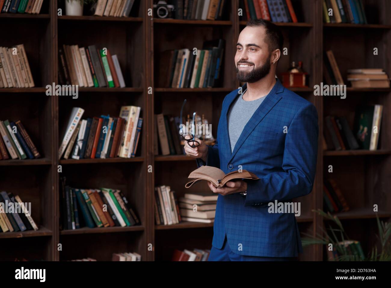 uomo d'affari bearded con gli occhiali in biblioteca con un taccuino in mano sorride. Giovane scrittore Foto Stock