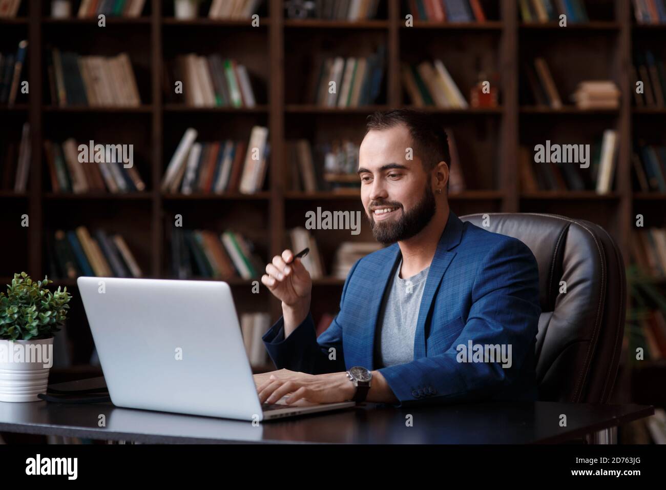 Un giovane uomo d'affari con gli occhiali sta lavorando su un computer portatile in un lussuoso ufficio nella biblioteca. Un uomo bearded in un vestito blu ad una scrivania sta digitando su un Foto Stock
