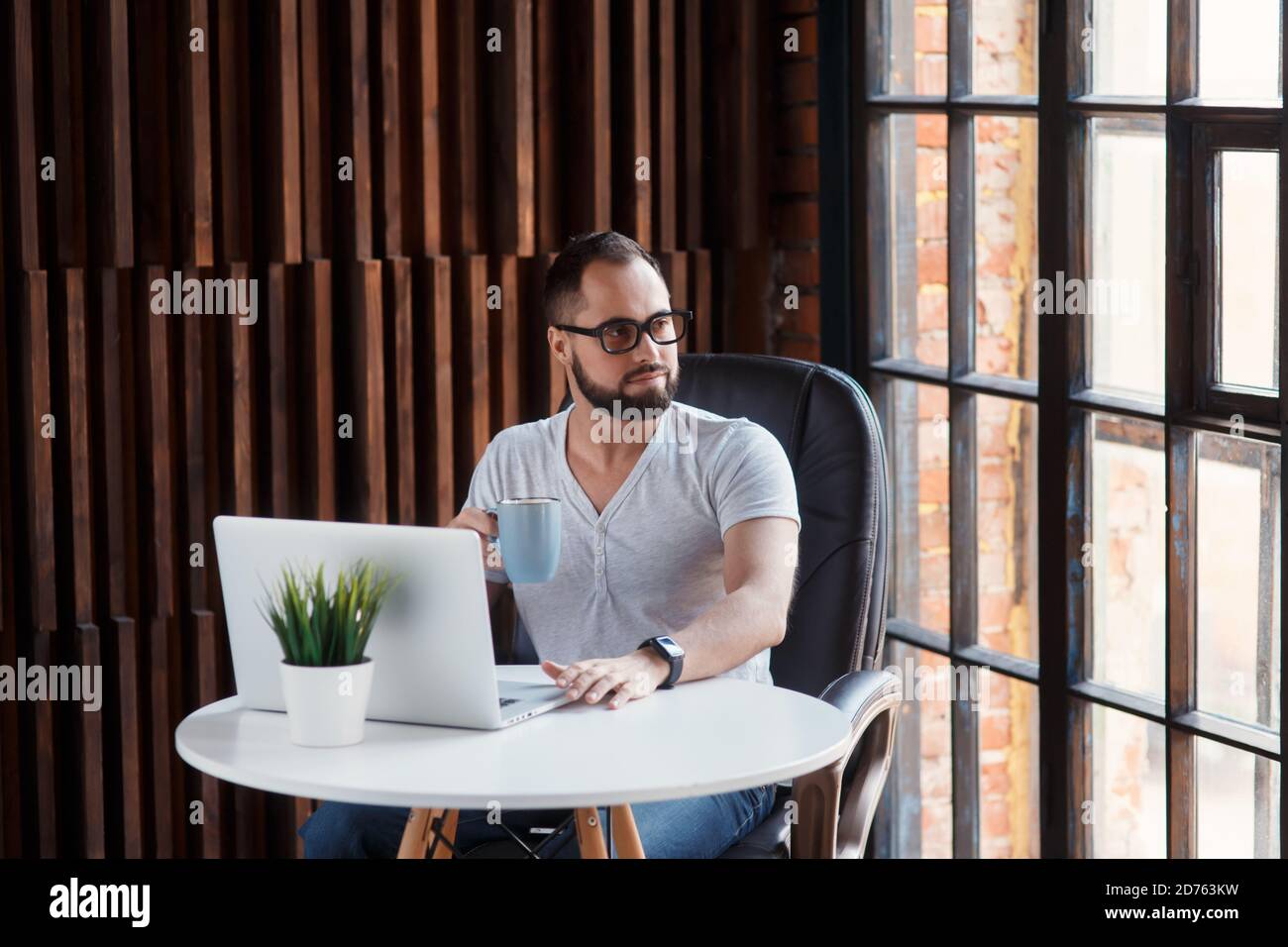 Giovane uomo d'affari sopportato di successo freelancer in ufficio coworking. Programmatore uomo felice sviluppatore in una t shirt bianca sorridente e bere caffè a. Foto Stock