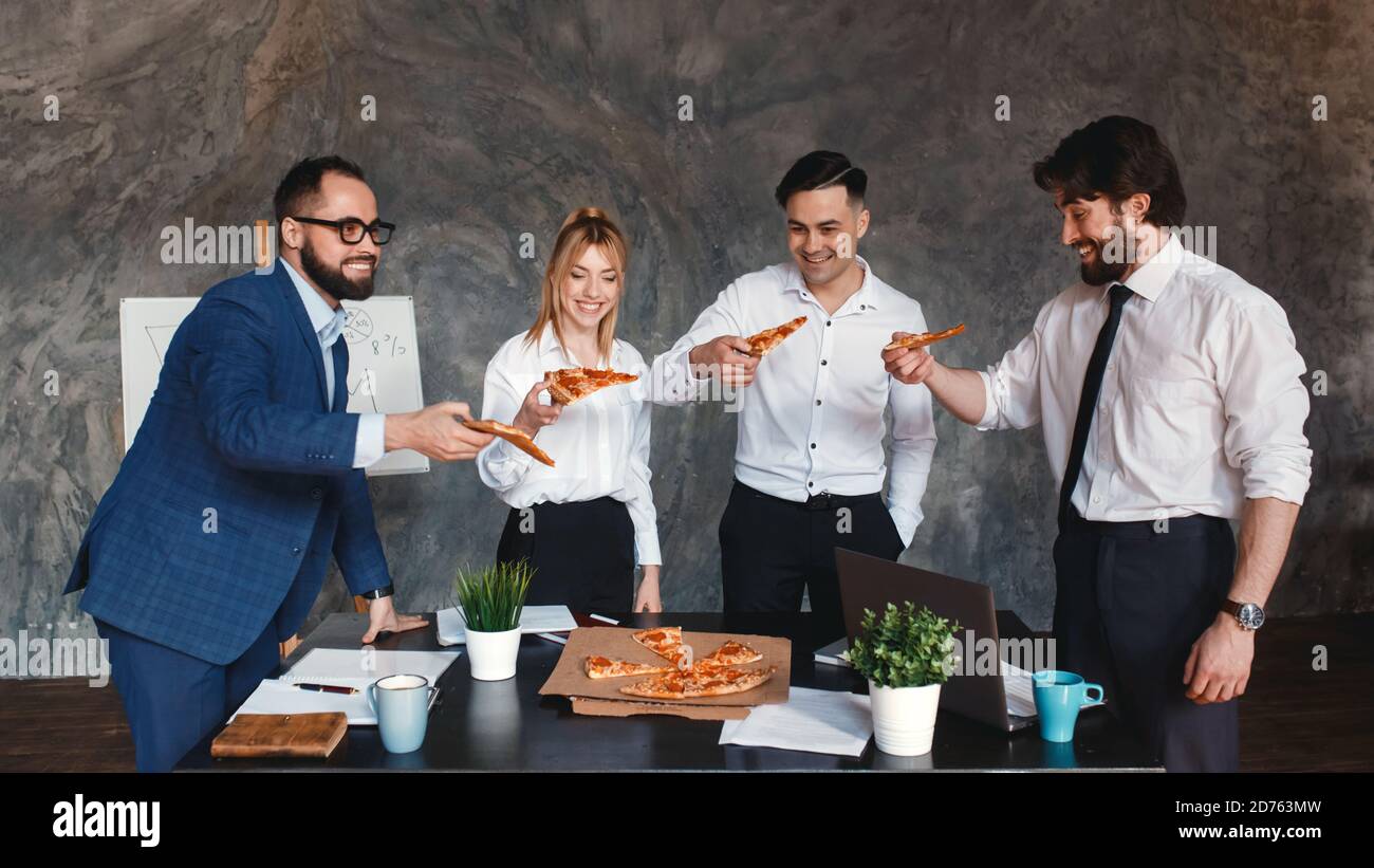 Felici i diversi colleghi trascorrono il lavoro pausa insieme mangiare take away consegna pizza in ufficio, sorridendo dipendenti multirazziali divertirsi, ridere e chattare Foto Stock