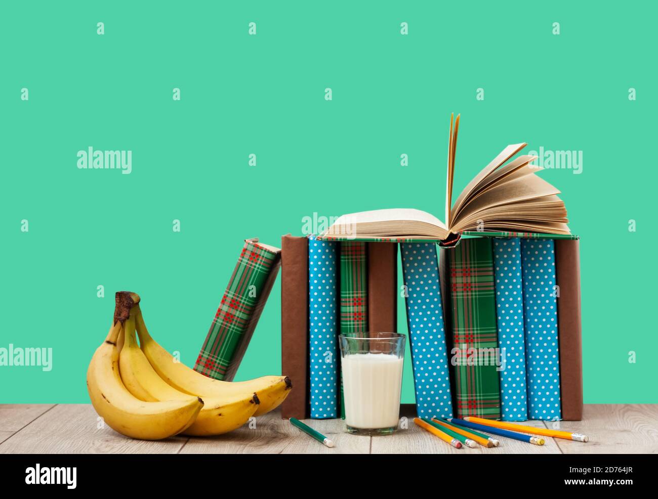 Apri il libro di testo in copertina colorata, banana e un bicchiere di latte su sfondo verde. Ritorno a scuola distanza casa Education.Quarantine concetto di s Foto Stock