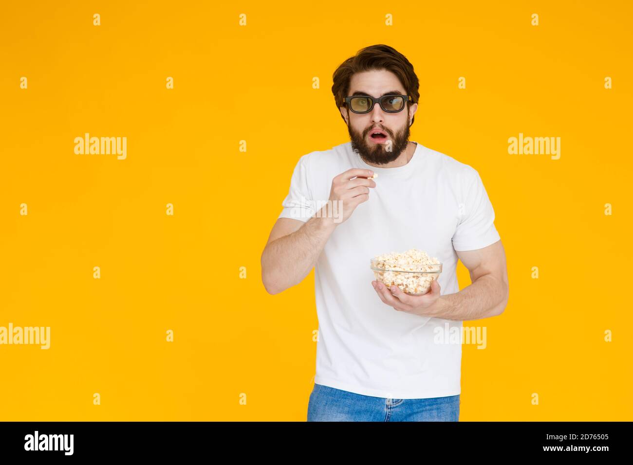 Ritratto Vogue giovane uomo in 3d bicchieri, t-shirt bianca guardando film, tenendo pop corn, tazza di soda isolato su sfondo giallo brillante. Persone Foto Stock