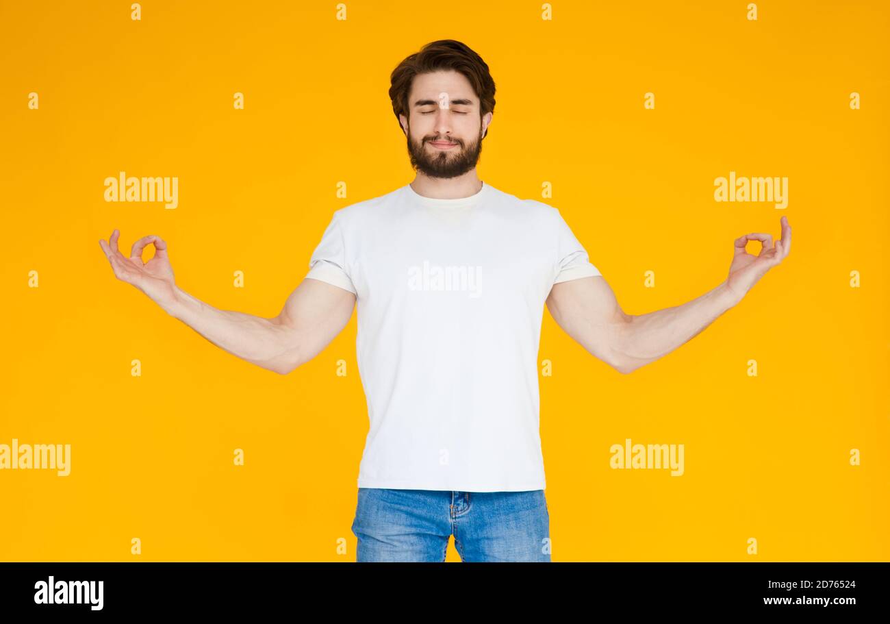 Sorridente giovane uomo bearded in camicia blu casual che posa isolato su sfondo giallo arancione parete. Concetto di stile di vita delle persone. Spazio di copia fittizio. Salto Foto Stock