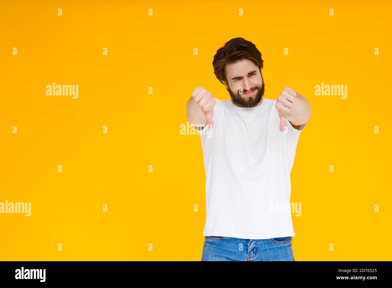 Giovane uomo caucasico isolato su sfondo giallo mostrando il pollice giù ed esprimendo dissimile. Foto Stock