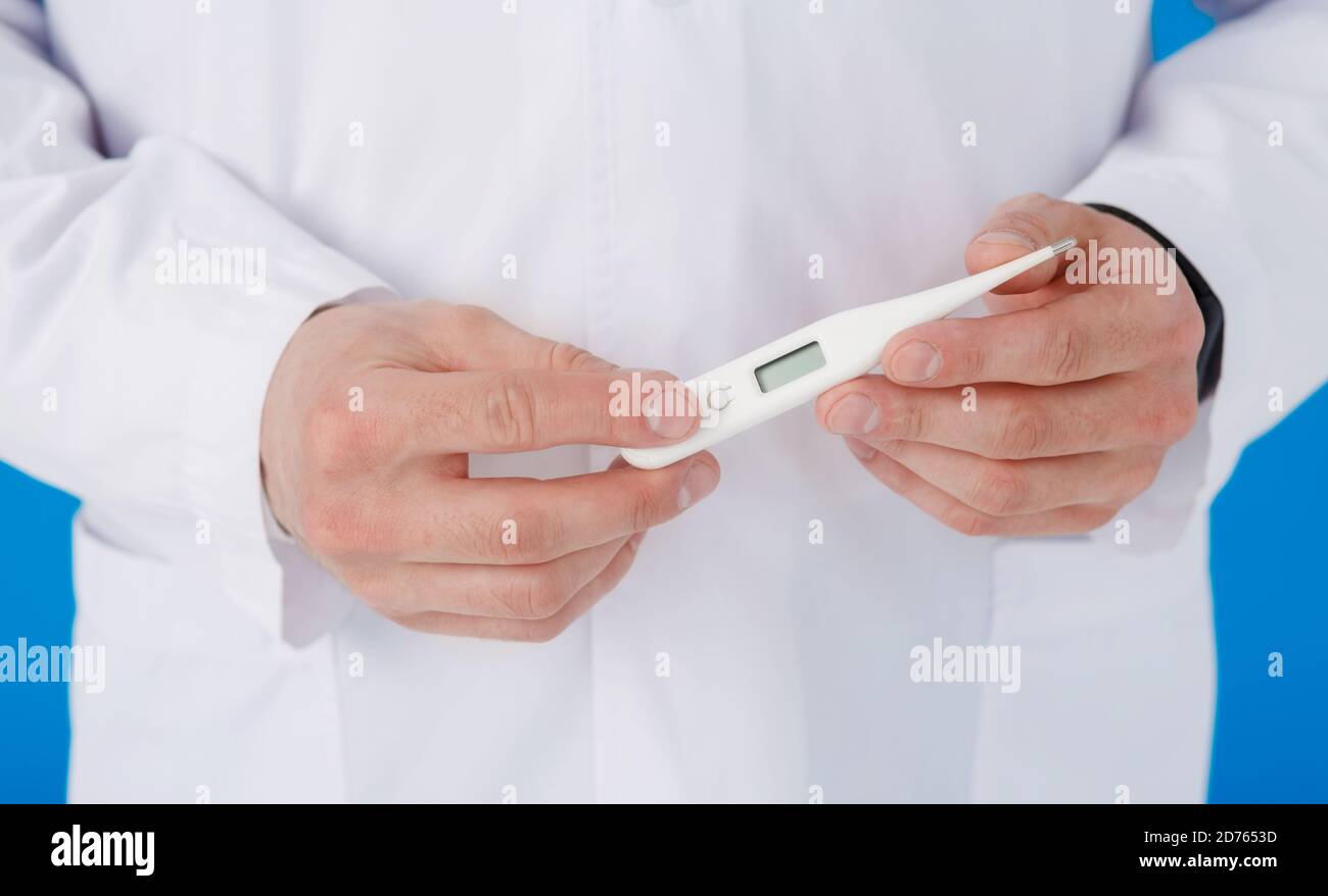 Primo piano vista del termometro in guanto blu di gomma vestito mano, petto uomo in abito medico bianco su sfondo sfocato Foto Stock