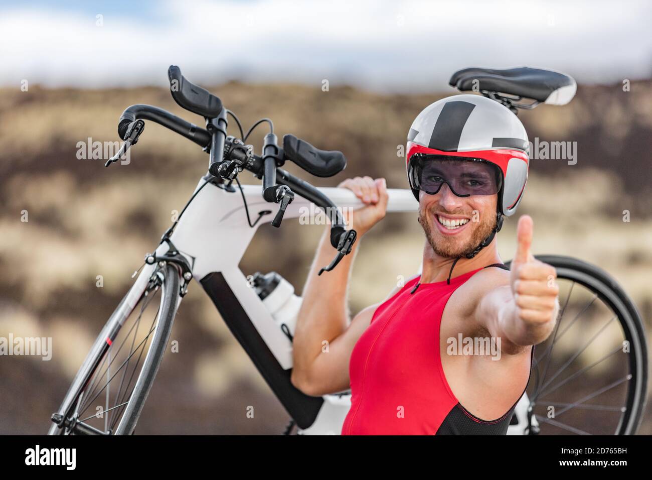 Triathlon bike - triatleta maschile ciclismo dando pollice su successo mano segno di tifo felice eccitato alla fotocamera. Montare l'uomo ciclista su professionale Foto Stock