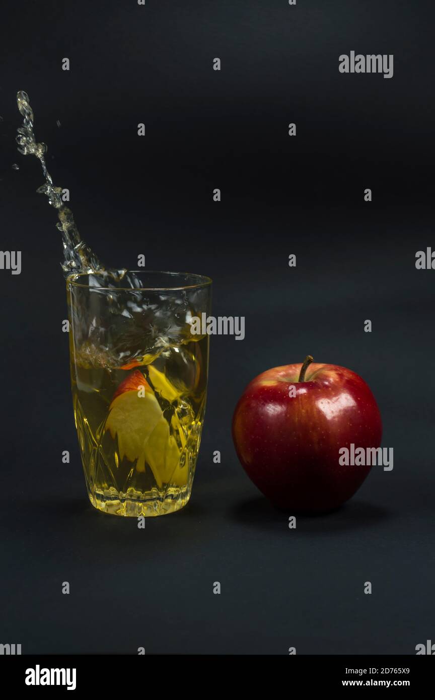 Fetta di mela gettata nel bicchiere che spruzzi succo di mela. Bella mela rossa accanto ad essa. Foto Stock