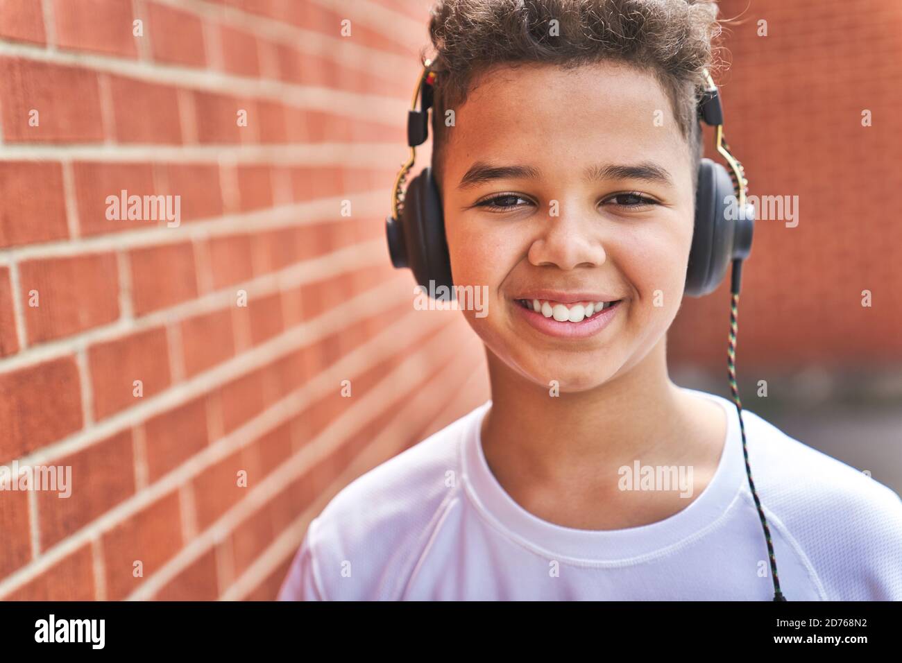 Bel ragazzo americano afro che ascolta musica al campo giochi della scuola muro di mattoni Foto Stock