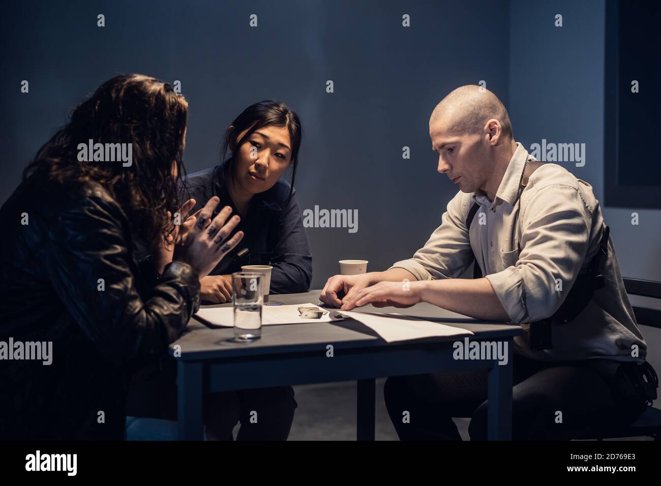 Un investigatore della polizia presso la stazione e il suo partner, una donna asiatica, presentano prove a un sospetto maschile in una sala di intervista. Foto Stock