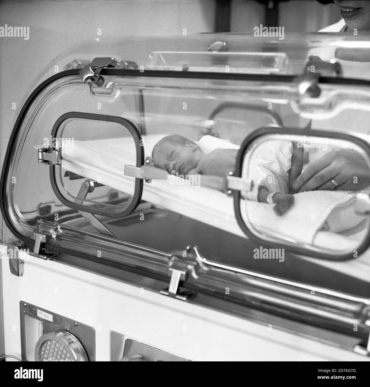 anni '70, storico, un neonato prematuro in un incubatore. Si può vedere quanto è piccolo il bambino prematuro confrontando la dimensione dei suoi piedi gambe con le dita della mano dell'infermiere visto nella figura a destra. Un incubatore è un'apparecchiatura medica che protegge la preemie da possibili infezioni e allergeni o da un eccessivo rumore di livelli di luce che potrebbero causare danni. Inoltre, vengono nutriti in incubatori per mantenerli caldi mentre l'umidità dell'aria è regolata in modo da essere un ambiente controllato e protettivo per la loro cura. Foto Stock