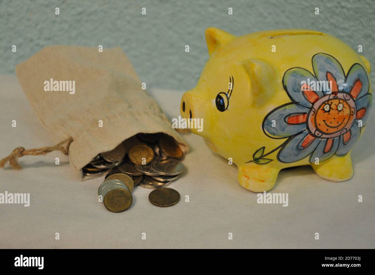 Piggy Bank, borsa di denaro in tela e monete su tavola bianca. Risparmio di denaro. Borsa piena di soldi e giallo Piggy Bank su sfondo blu. Foto Stock