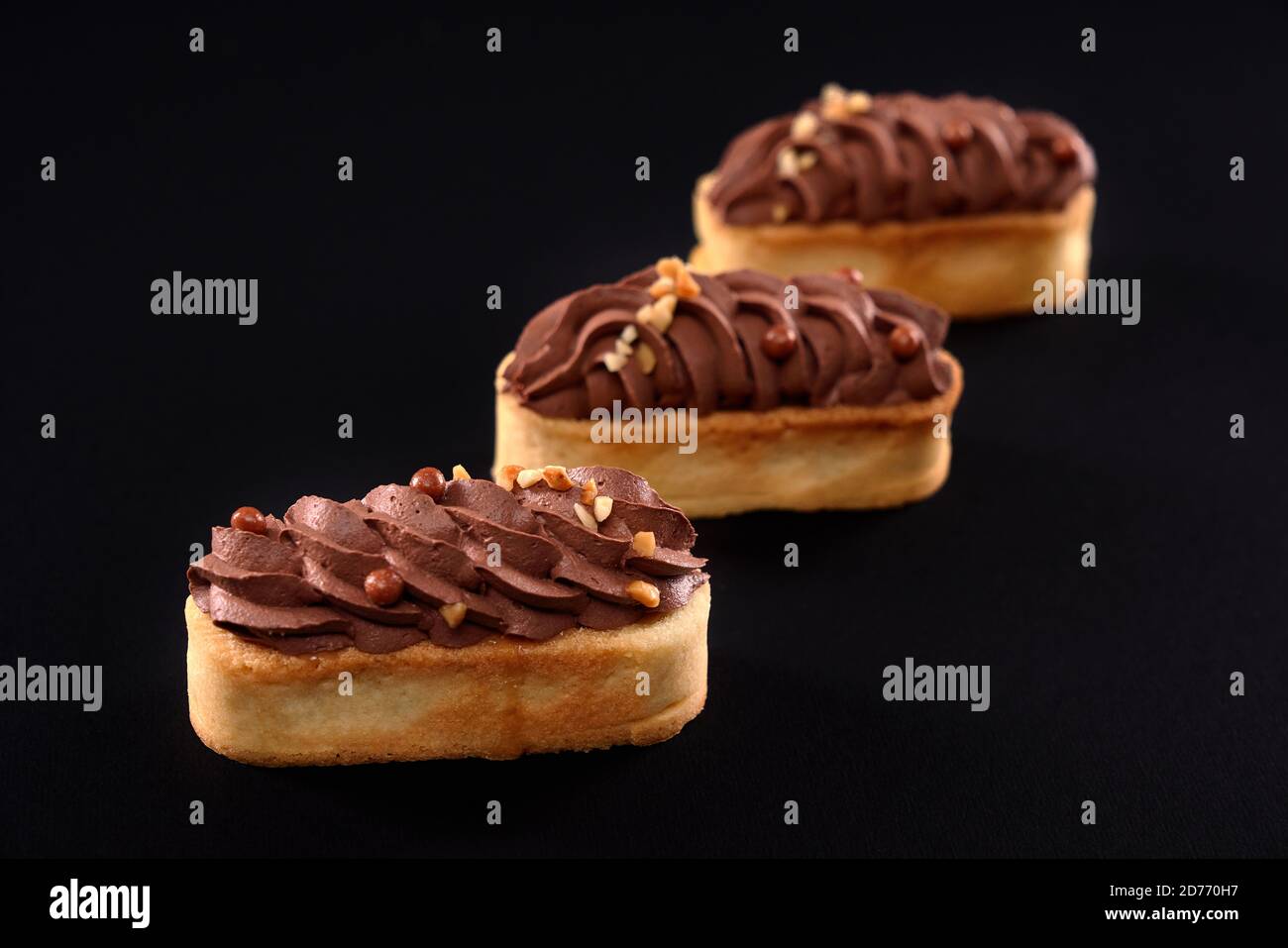 Biscotti frollini con mascarpone panna di cioccolato marrone montata sulla parte superiore. Tre dolci freschi fatti in casa isolati su sfondo nero. Concetto di dolci, dessert. Foto Stock