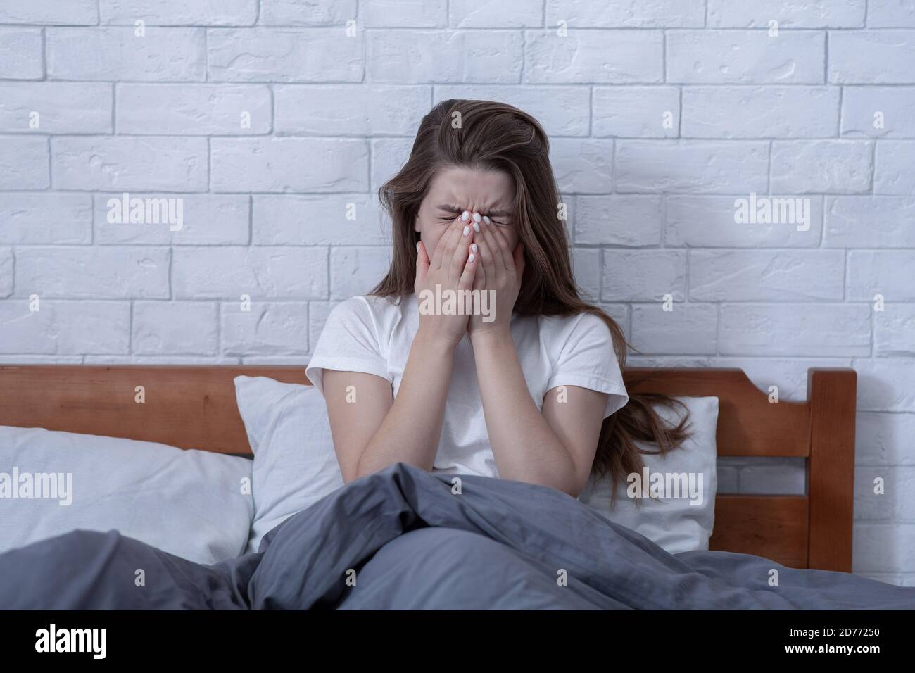 Donna millenaria depressa seduta e piangendo con le mani sul viso in camera da letto Foto Stock