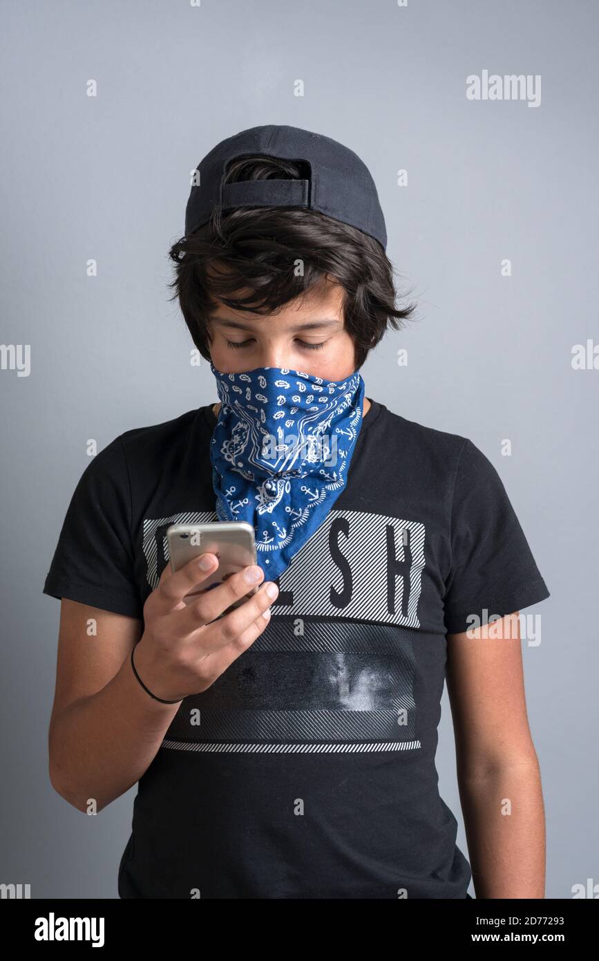Il ragazzo adolescente indossa il bandana come maschera facciale sul suo telefono Foto Stock