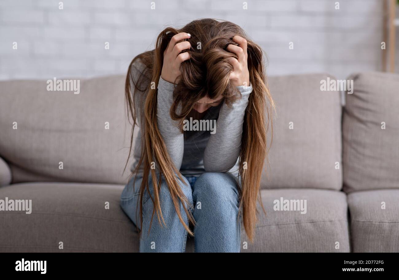 Disperata giovane donna seduta testa in mani sul divano e piangendo, panorama Foto Stock