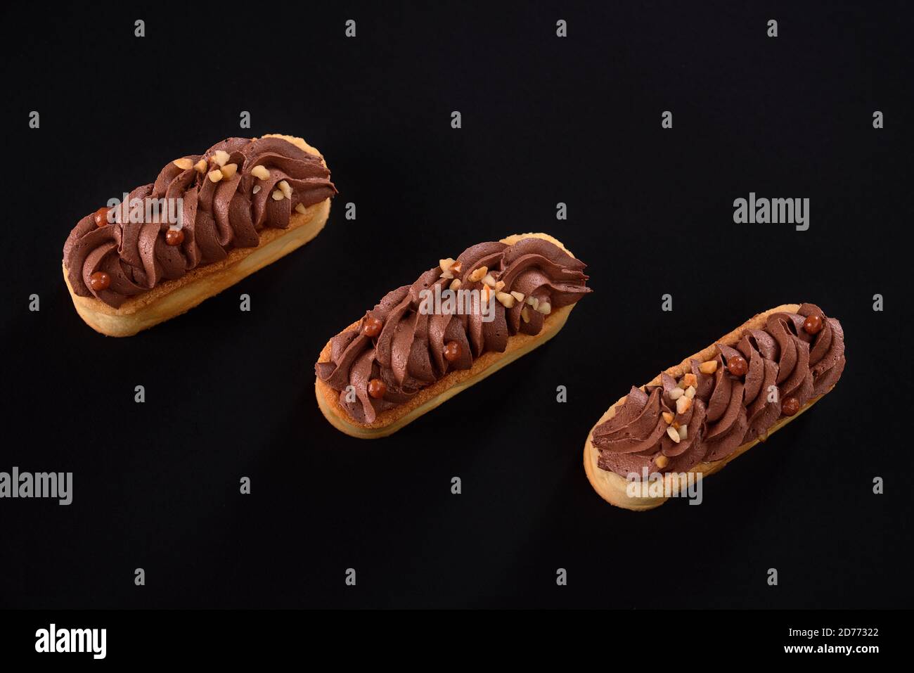 Biscotti frollini con panna di cioccolato marrone montata con mascarpone. Vista dall'alto di tre dolci freschi fatti in casa isolati su sfondo nero. Concetto di dolci, industria alimentare. Foto Stock