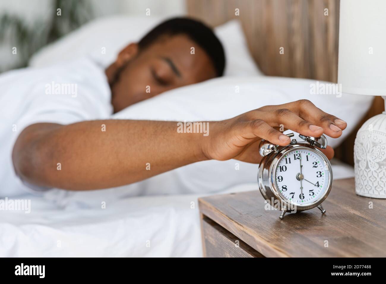 Uomo nero assonnato spegnimento sveglia sdraiata nel letto Foto Stock