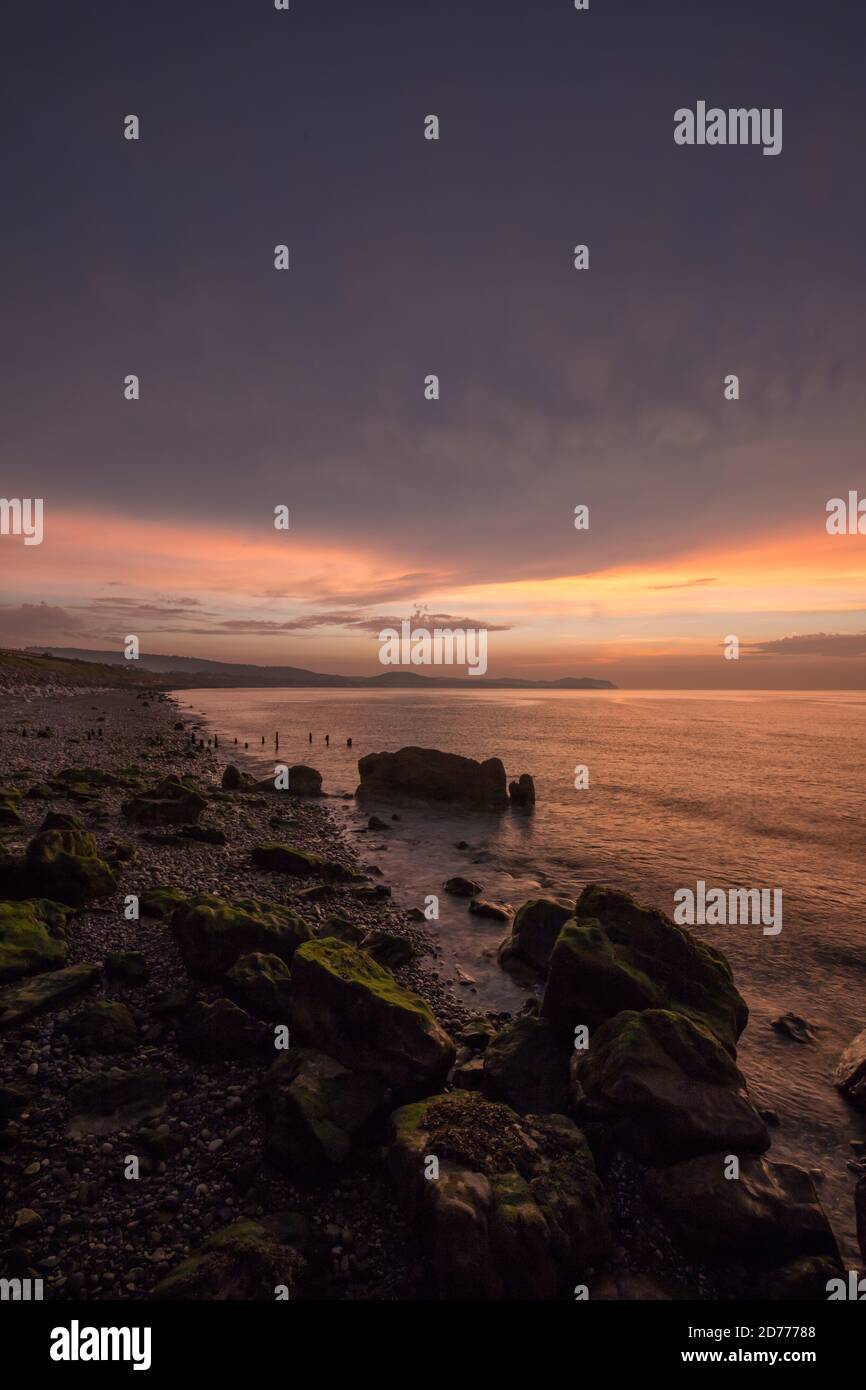 Tramonto dell'ora d'oro alla baia di Colwyn, Galles del Nord. Cielo caldo e dolci onde lungo una costa rocciosa Foto Stock