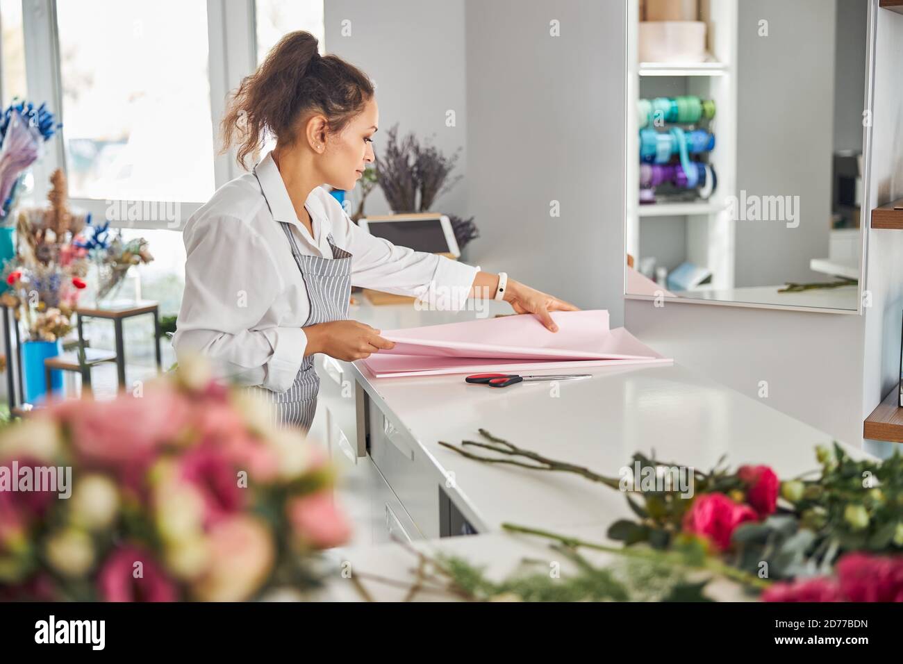 Donna bruna entusiasta che tocca carta regalo-avvolgente sul tavolo Foto Stock