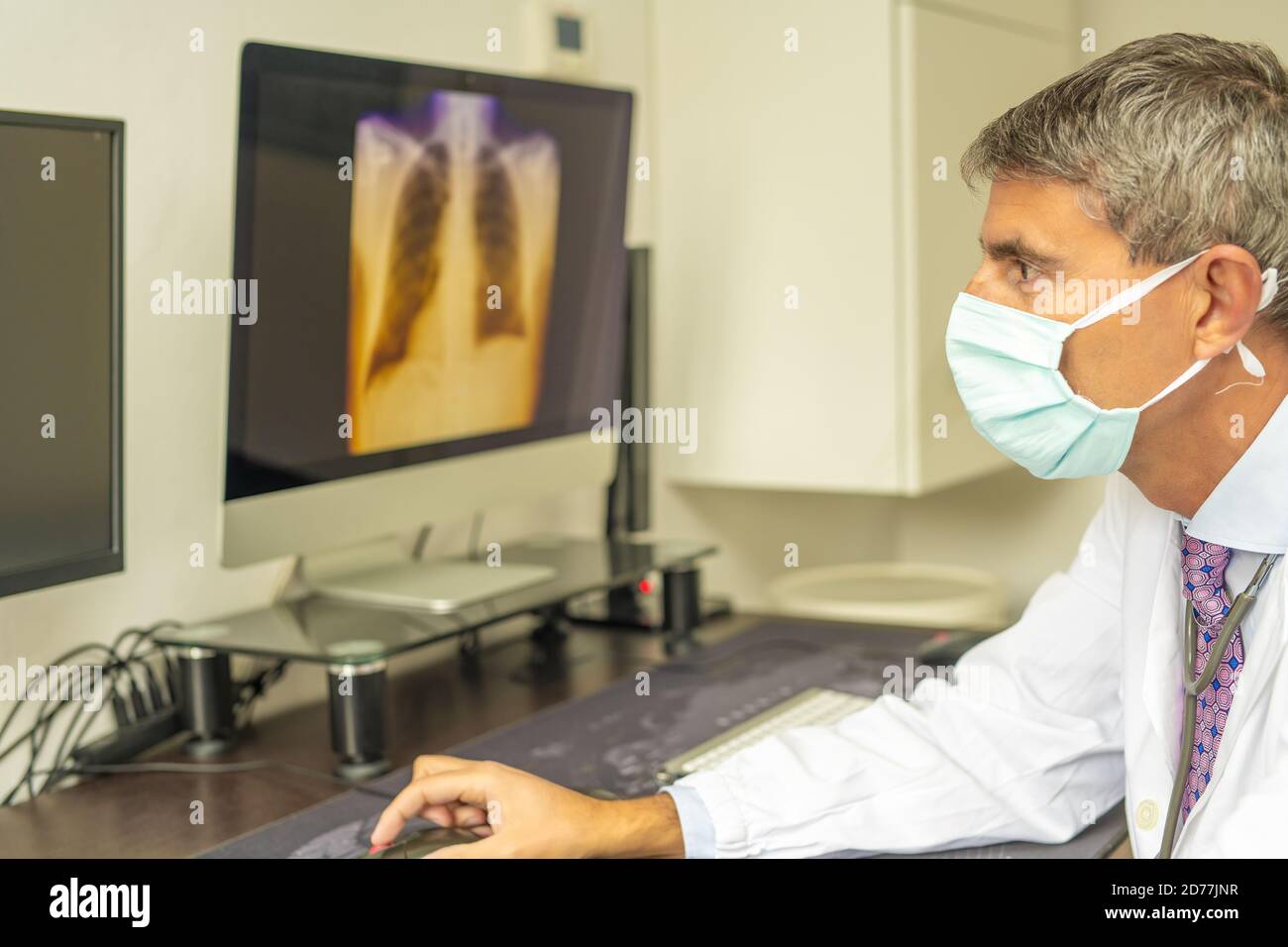 Medico di sesso maschile che indossa la maschera nel reparto covid-19 guardando i raggi X del paziente sullo schermo del computer. Foto Stock