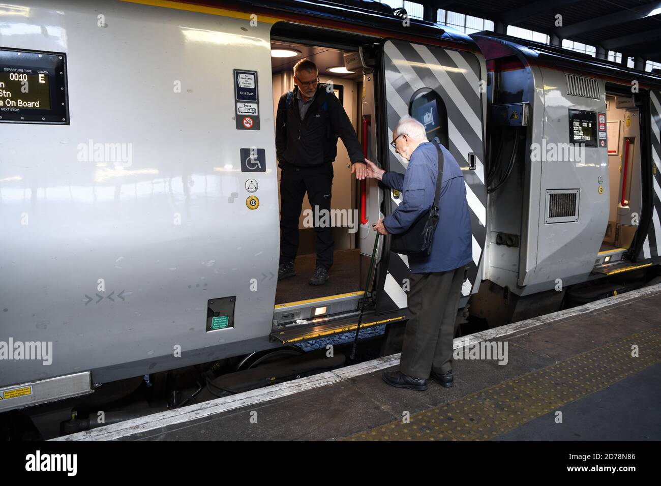 L'uomo aiuta i gentiluomini anziani a salire a bordo del treno Virgin a Euston London. Foto Stock