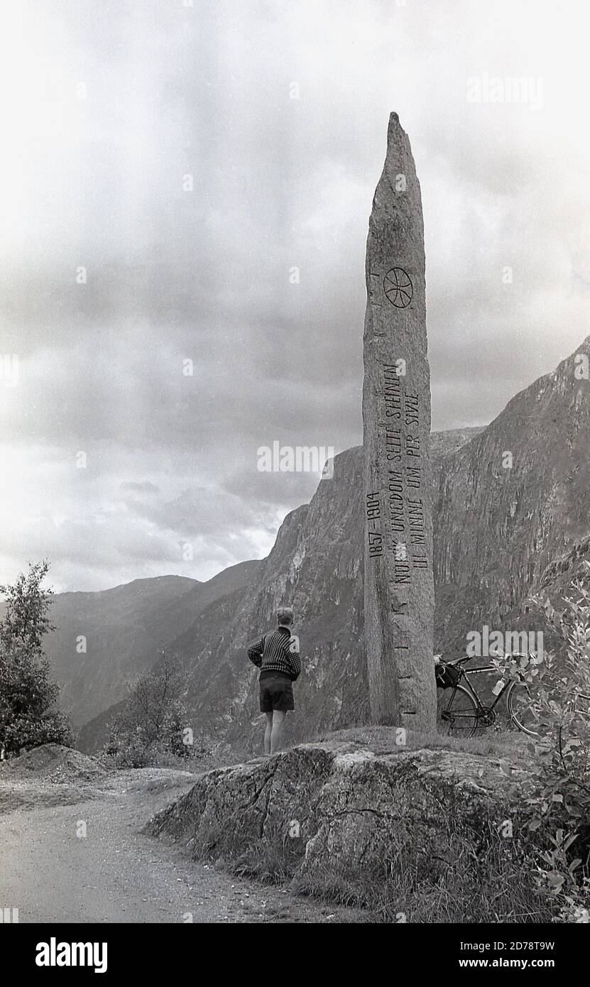 Anni '50, storico, cicloturando le Alpi svizzere, un ciclista maschile nelle Alpi che si trova accanto a una statua di pietra, dicendo 'Norsk Ungdom Seite...... Foto Stock