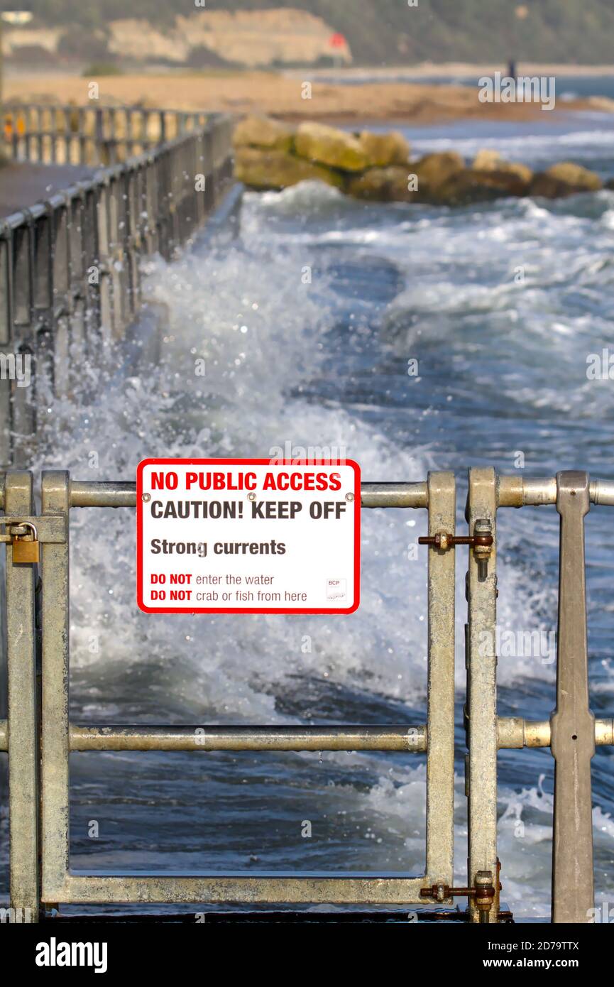 WarningSign su Mudeford Quay Christchurch UK avvertimento di forti correnti e nessun accesso pubblico con ondulato, mare pesante in background Foto Stock