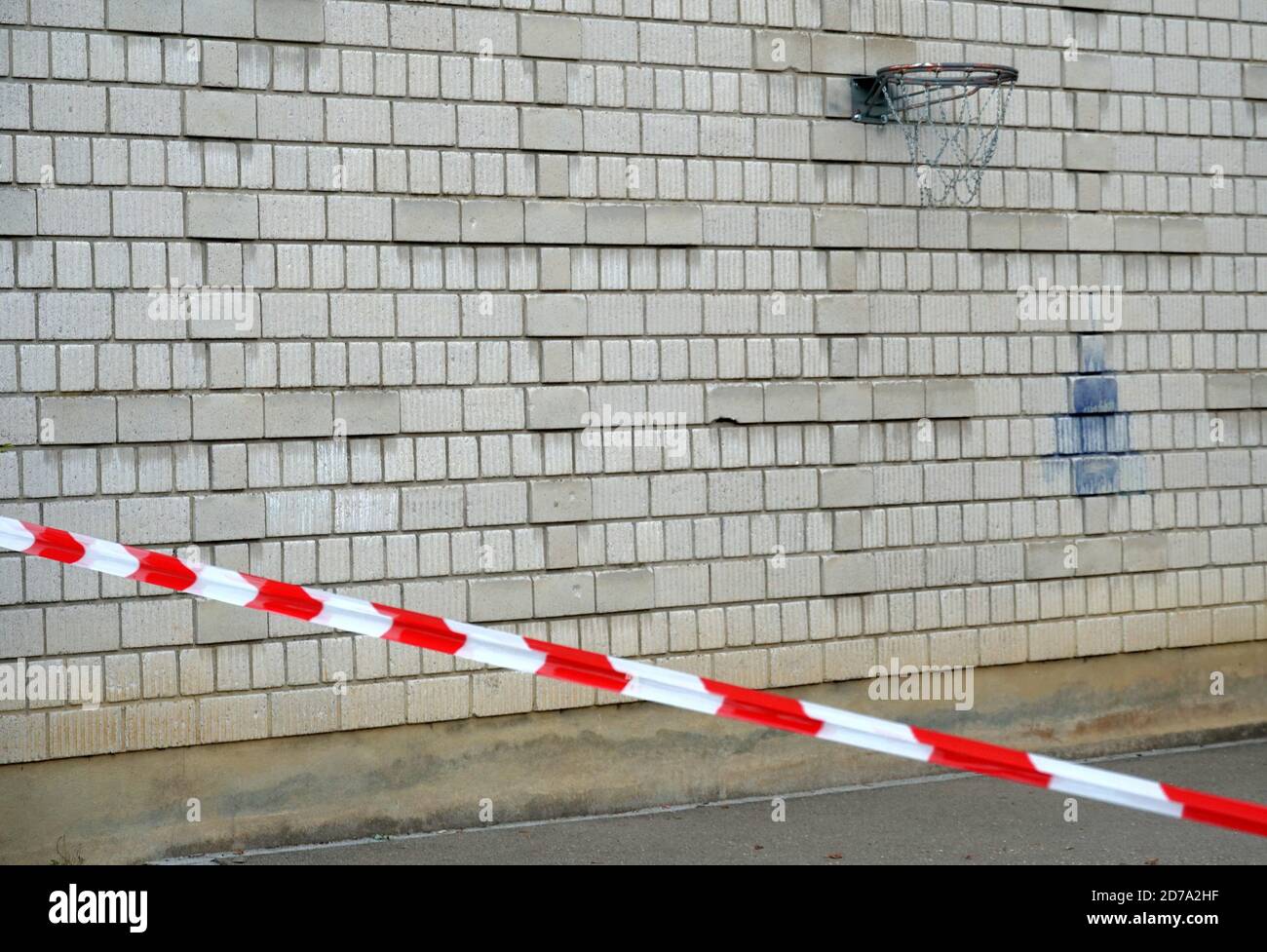 Cesto di basket attaccato su un muro di mattoni. In primo piano c'è un nastro barriera di bianco rosso come misura preventiva nella seconda ondata di corona Foto Stock