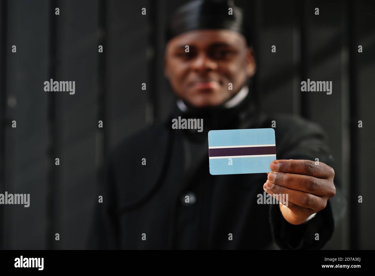 Uomo africano indossare durag nero tenere bandiera Botswana a mano isolato sfondo scuro. Foto Stock