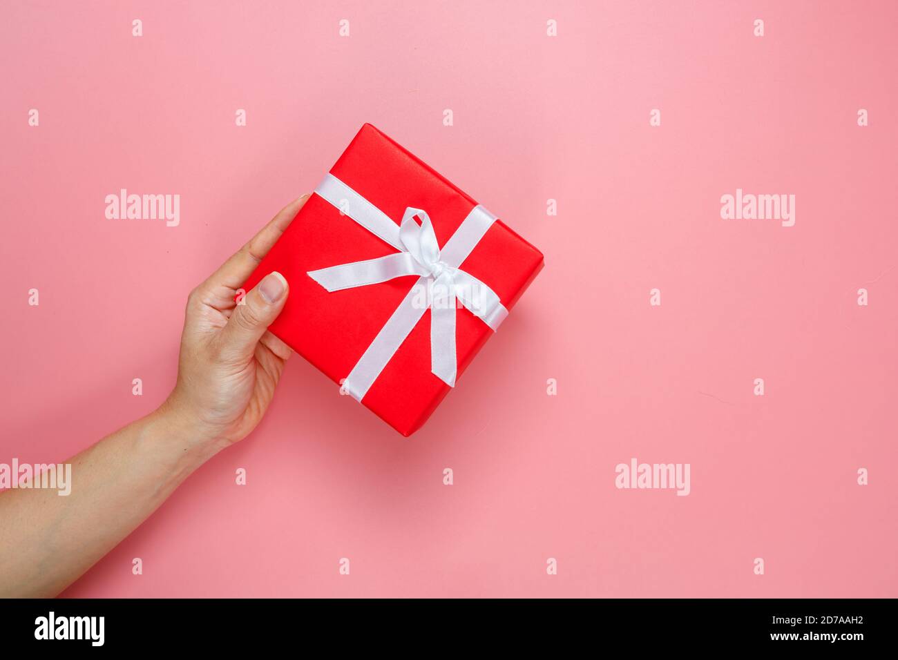 Piatto posa di mani donna che reggono regalo avvolto e decorato con arco isolato su sfondo rosa con spazio copia. San Valentino amore. Tema compleanno. Foto Stock