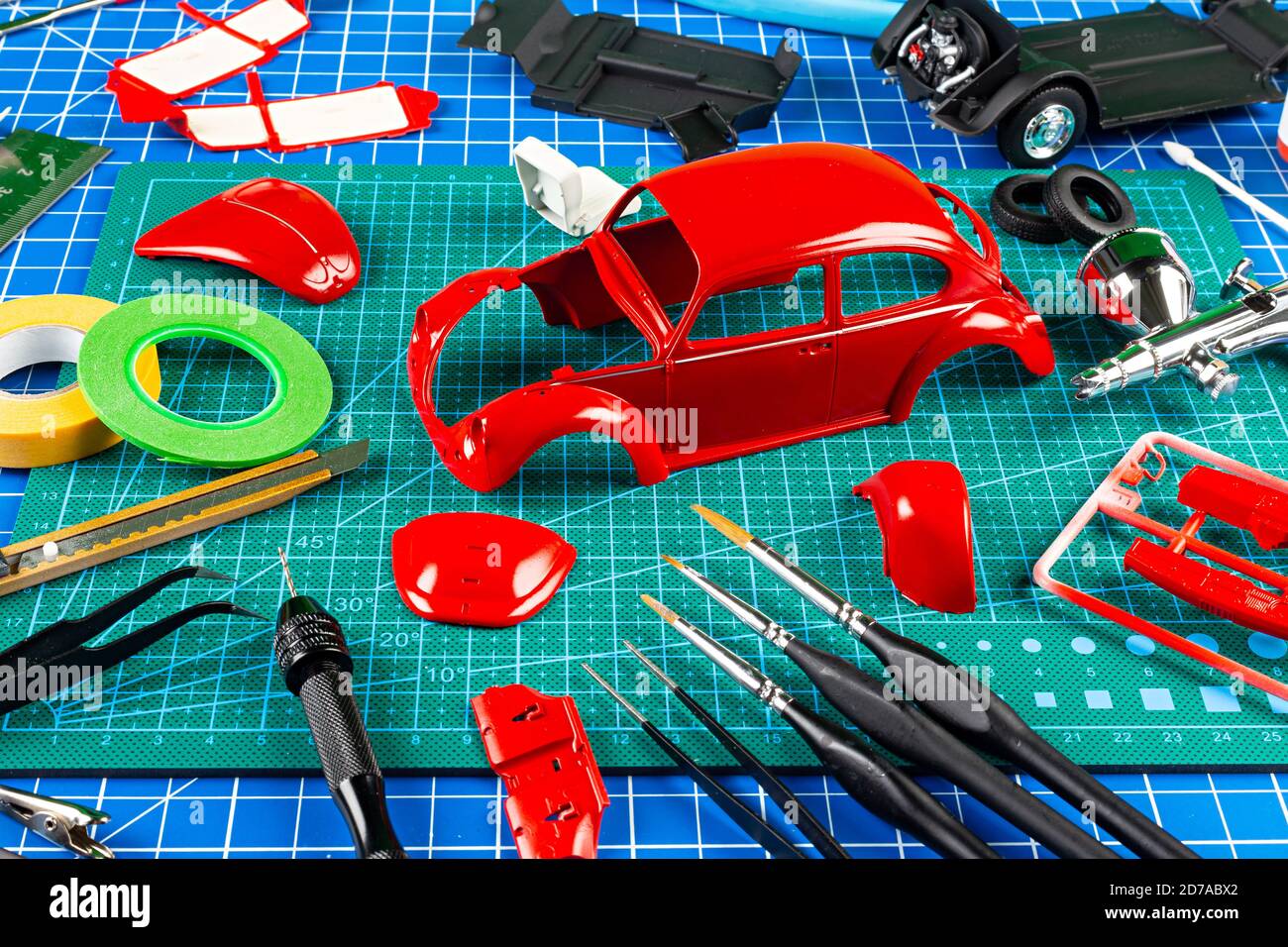 vista da tavolo montaggio e verniciatura di un modello in scala retrò rossa veicolo concept background. strumenti di modellazione pistola aerografo kit vernice parti blu verde c Foto Stock