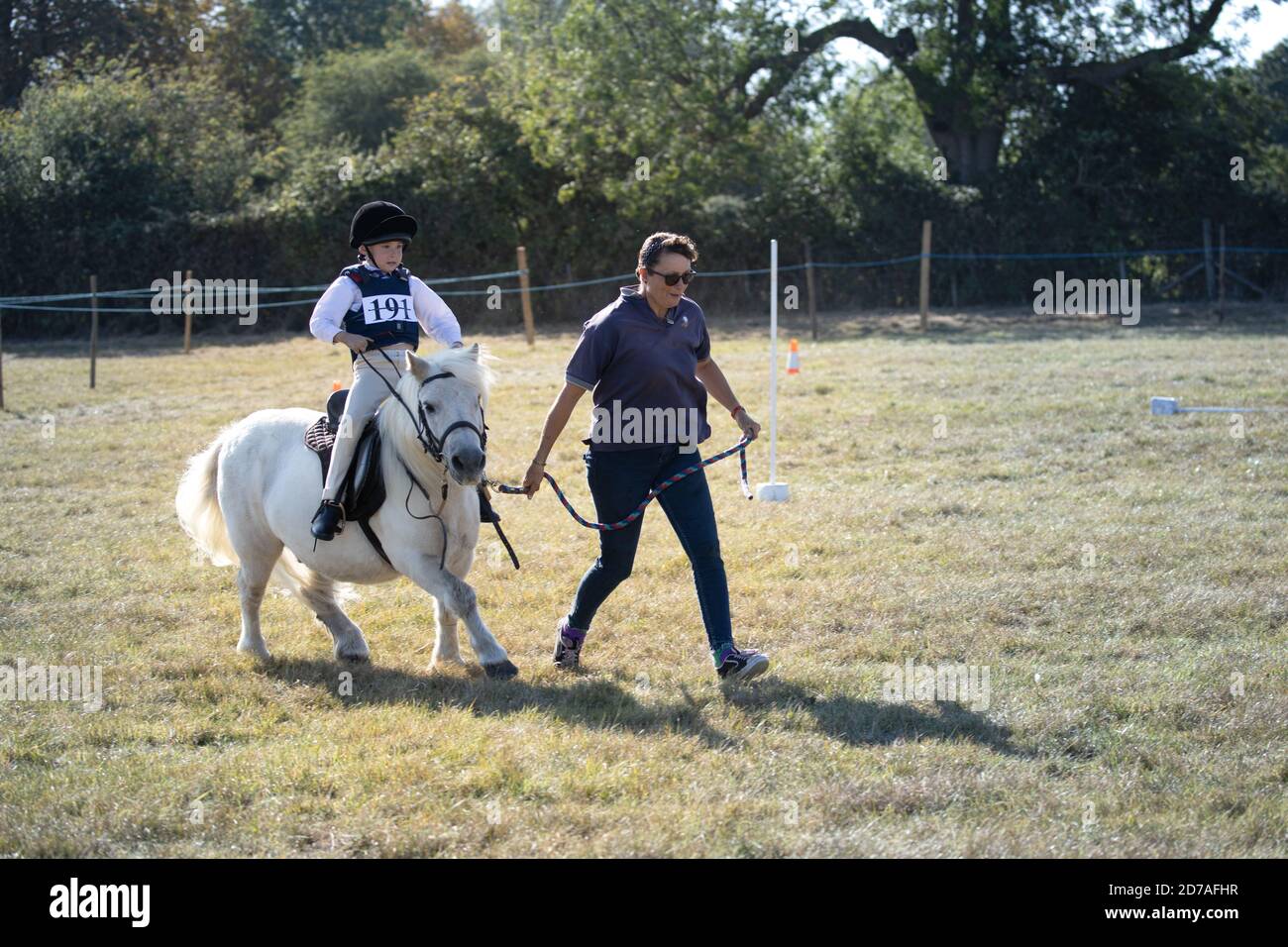 Donna che conduce piccolo pony grigio e determinato giovane pilota Al locale gara di equitazione gymkhana Inghilterra Foto Stock