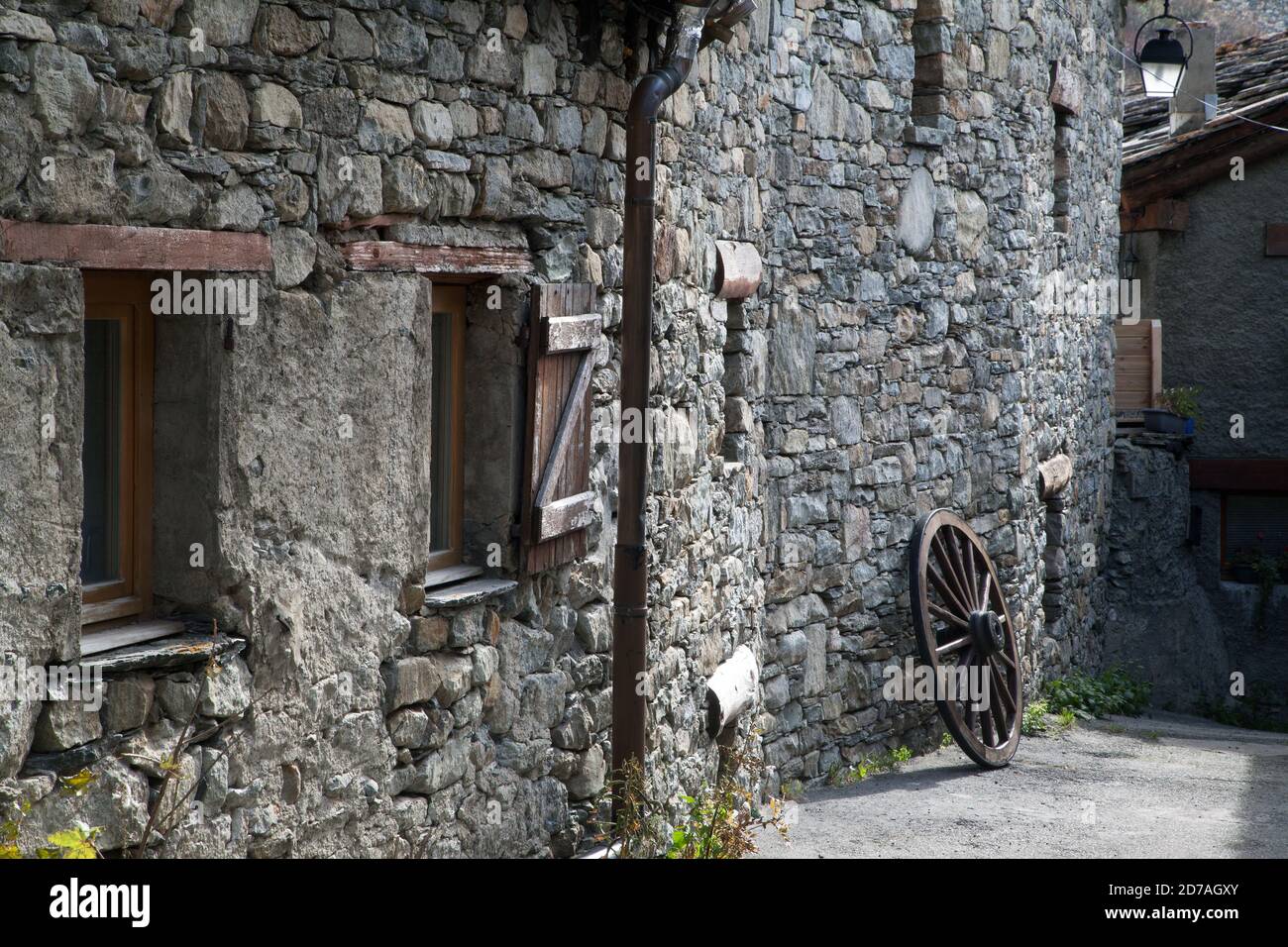 una vecchia ruota che poggia contro il muro e le finestre di Una vecchia casa in pietra a Bonneval-sur-Arc Haute-Maurienne Savoia Francia Foto Stock