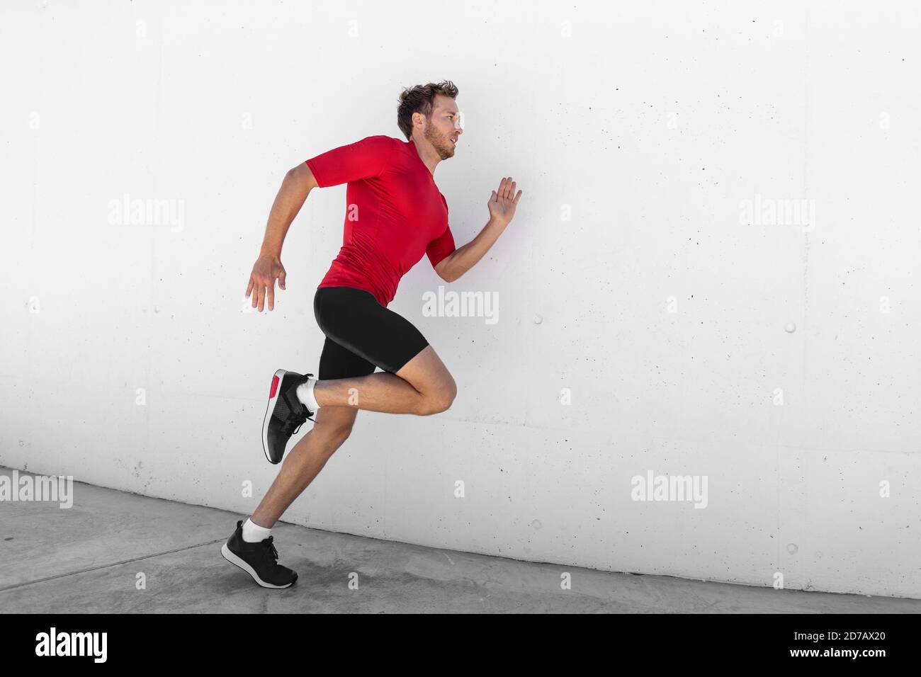 Running uomo jogging profilo veloce lateralmente contro bianco parete sfondo esterno. Atleta maschile allenamento sano stile di vita attivo Foto Stock