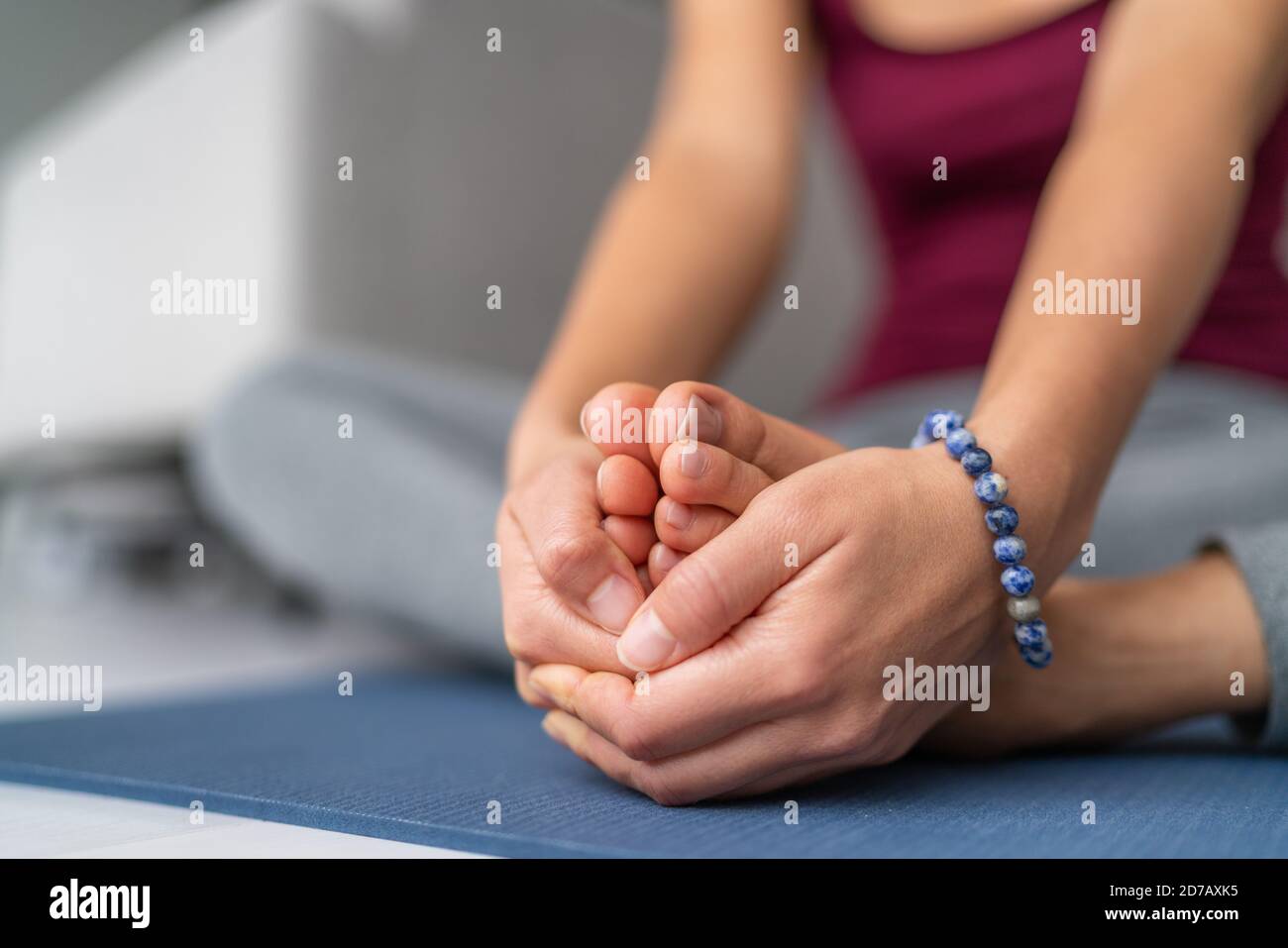 Donna che stretching Yoga su tappetino per esercizi a casa. Seduta gamba farfalla stretch tenendo suole di piedi insieme con le mani Foto Stock