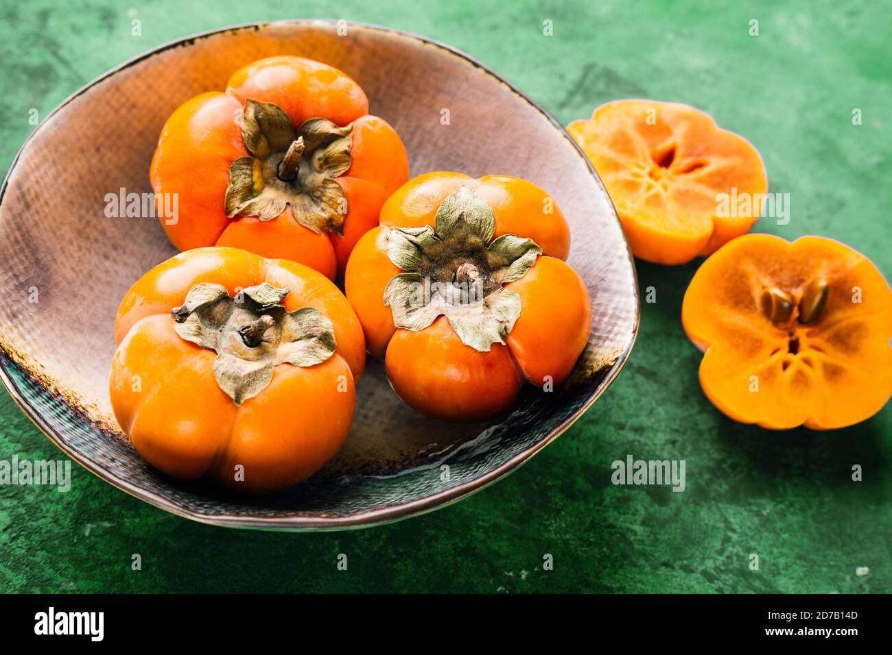 persimmon in una piastra di ceramica su sfondo verde Foto Stock