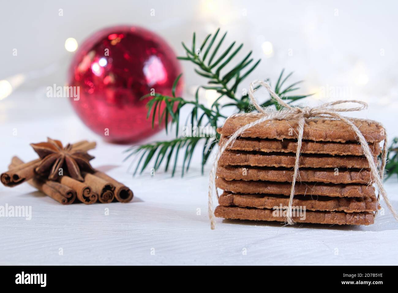 Avvento e Natale umore, speculoos impilati con un nastro da imballaggio legato, decorato su un tavolo di legno bianco sullo sfondo una palla di natale rosso Foto Stock