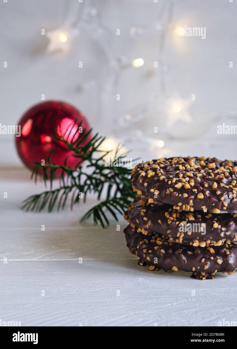 Avvento e umore natalizio, Elisenlebkuchen con glassa al cioccolato e nocciole, su un tavolo di legno bianco sullo sfondo una palla rossa di natale Foto Stock