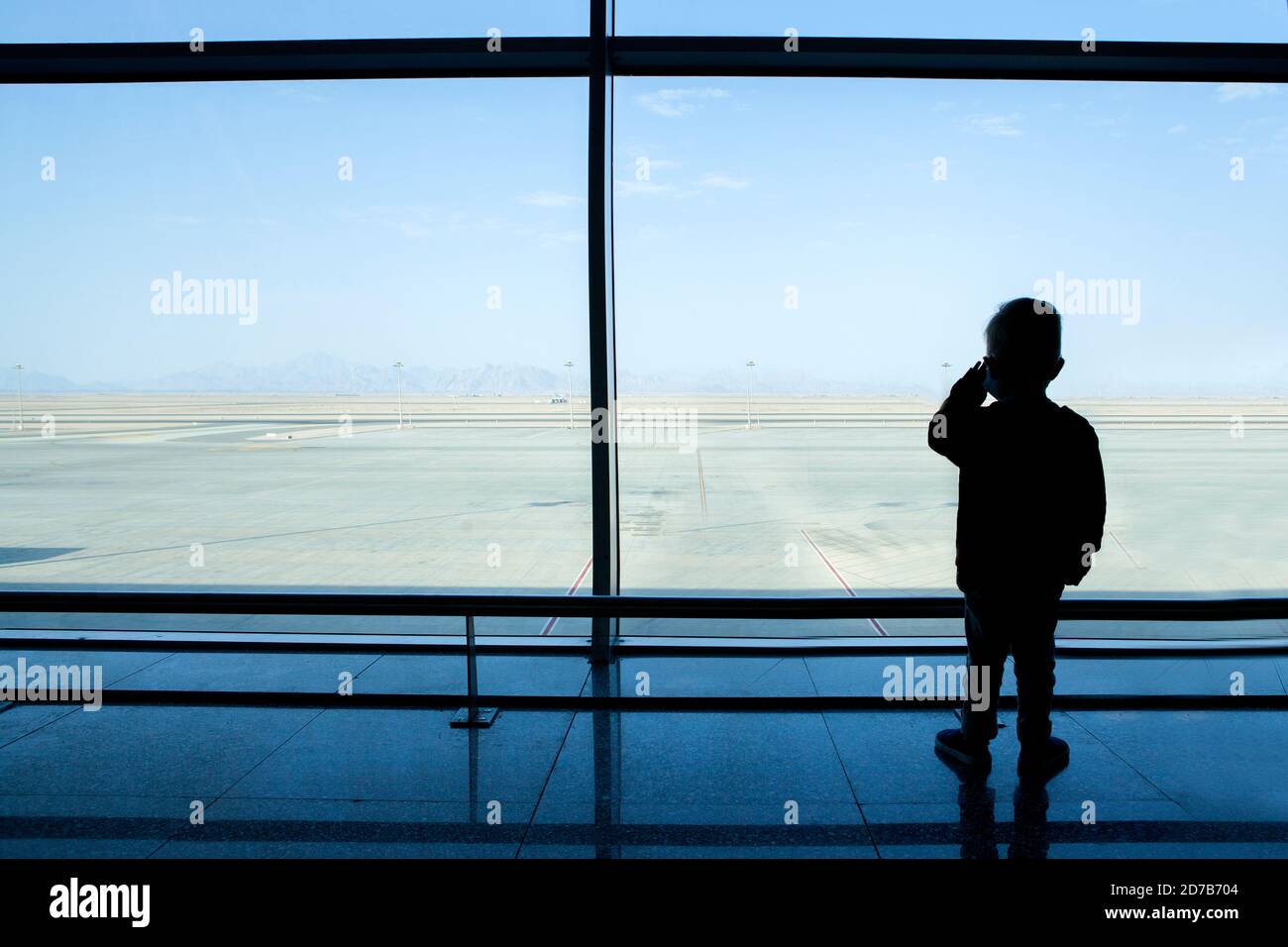 Ragazzo che guarda attraverso una finestra all'aeroporto vuoto. Foto Stock