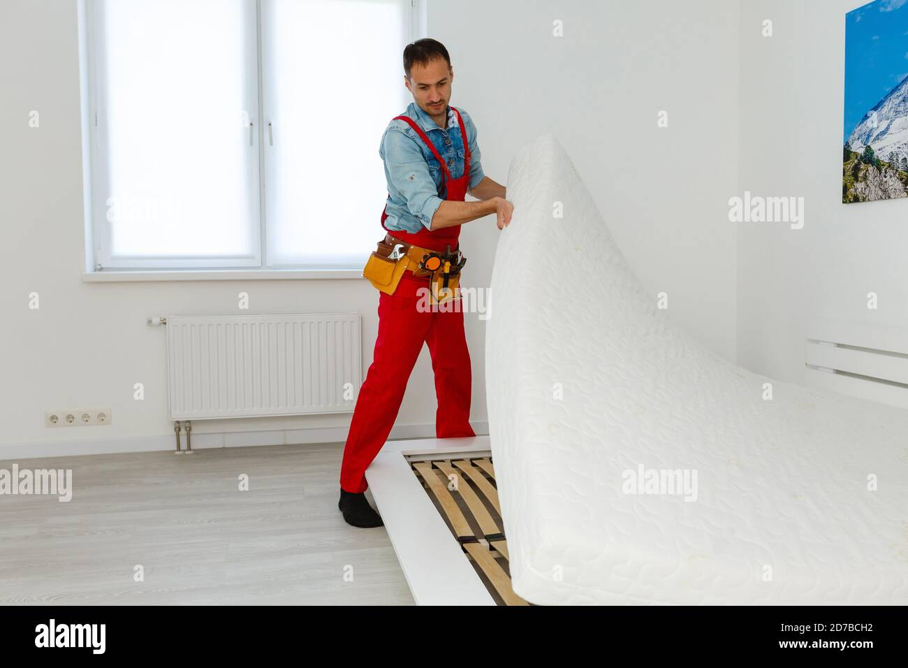 Le mani dell'uomo che lavorano con una chiave esagonale. Montaggio di mobili. Tavola di legno di un letto. Primo piano. Foto Stock