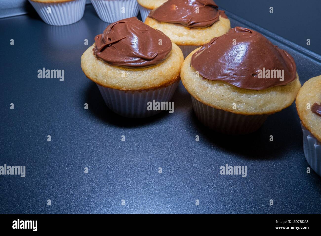 I cupcake bianchi con glassa di cioccolato si siedono in una padella Foto Stock