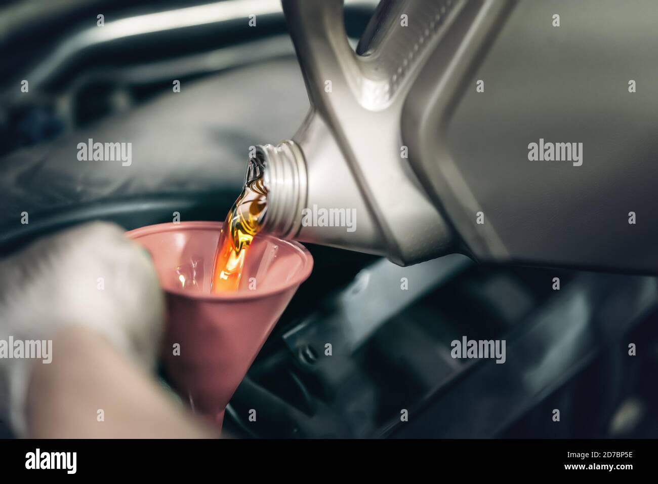 L'operatore versa il nuovo olio motore sintetico dal canister nel motore dell'auto al momento dell'intervento. Foto Stock