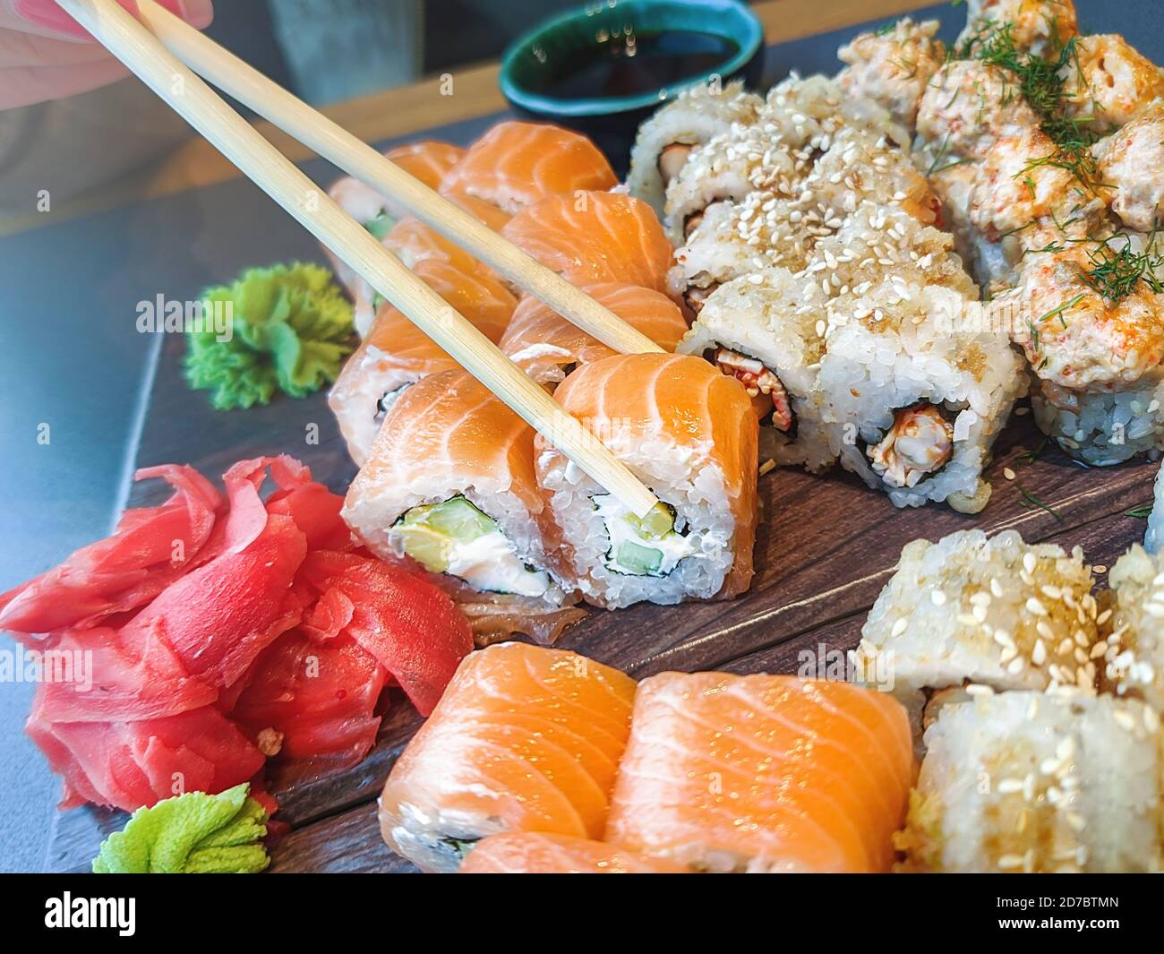 La mano della ragazza tiene i chopsticks e mangia i vari panini del sushi nel ristorante. Foto Stock