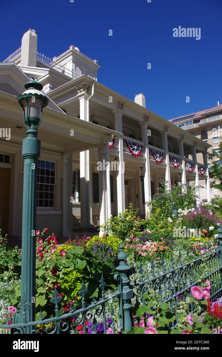 Salt Lake City, UT--12 luglio 2012; casa pioniera in legno centro con giardino di fiori dietro recinzione di ferro verde e ex casa di Brigham Young leader di Foto Stock