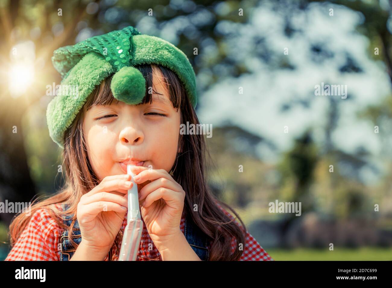 Piccolo felice School girl giocando parte soffiare il clacson per il suo compleanno nel giardino in estate. Stili di vita dell'infanzia concetto. Foto Stock
