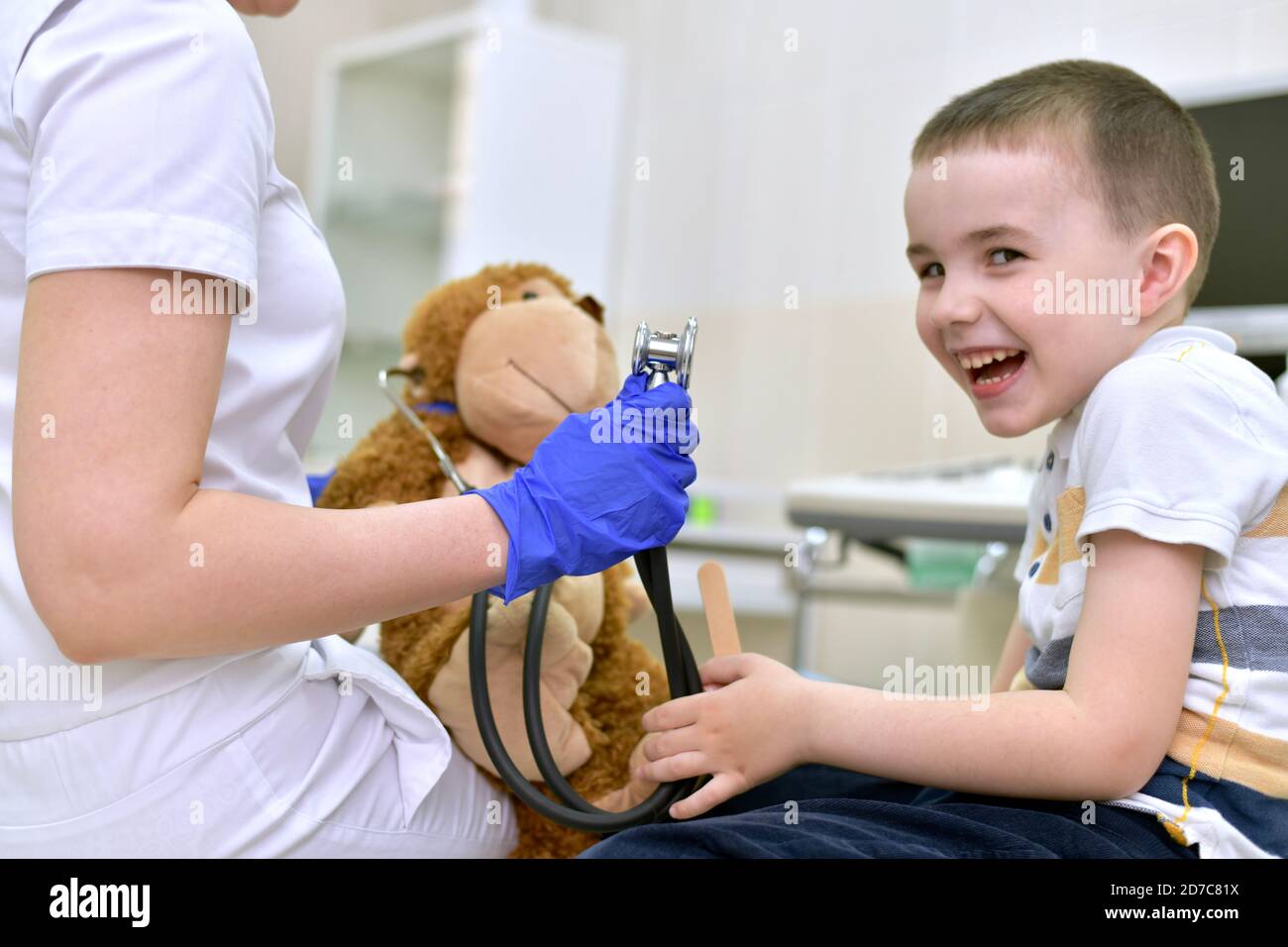 Il bambino paziente ride alla reception del medico, che con una scimmia giocattolo sta per ascoltare il respiro. Foto Stock