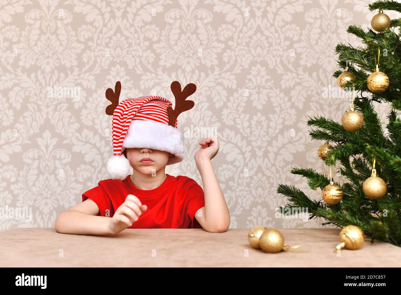 Un ragazzo in un cappello, vestito negli occhi. Un uomo sconcertato si siede all'albero di Natale. Foto Stock